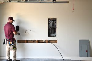 An electrician installing an electrical charging station on a wall in a garage with an open electrical panel visible