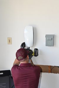 An electrician kneeling in a garage to complete an electrical vehicle charging station installation