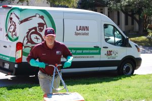 An ABC employee pushing lawn equipment in front of an ABC van, working on a customer's yard