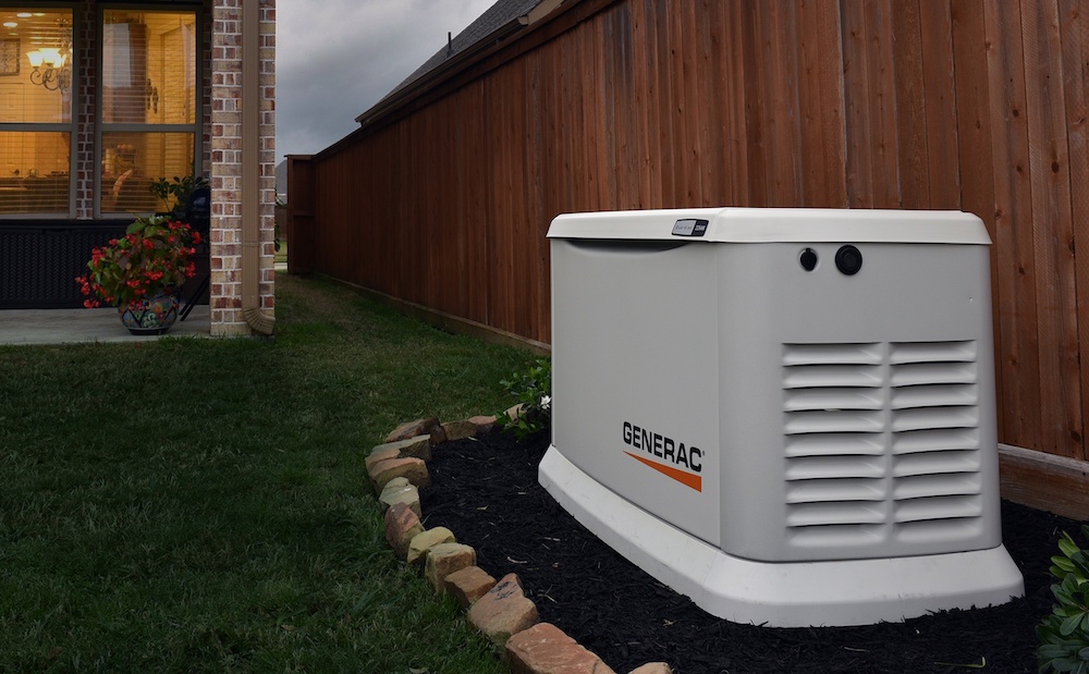 A Generac brand standby generator along a fenceline