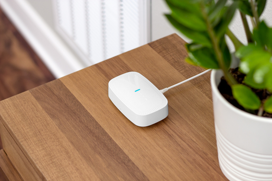 A smart AC sensor on a table, beside a plant