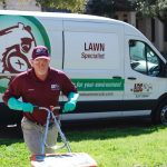 An ABC employee pushing lawn equipment in front of an ABC van, working on a customer's yard