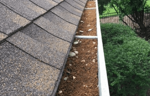 a gutter running along side a roof before ABC specialist have cleaned it; it is filled with dirt and debris. 