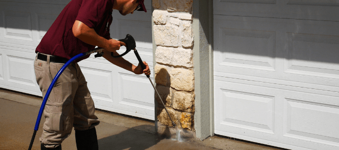a homeowner pressure washing the stone exterior of their home