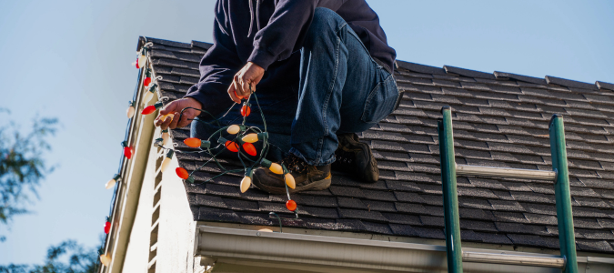 Person installing Christmas lights on roof