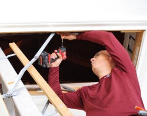 an ABC handyman using a drill on an attic stairwell