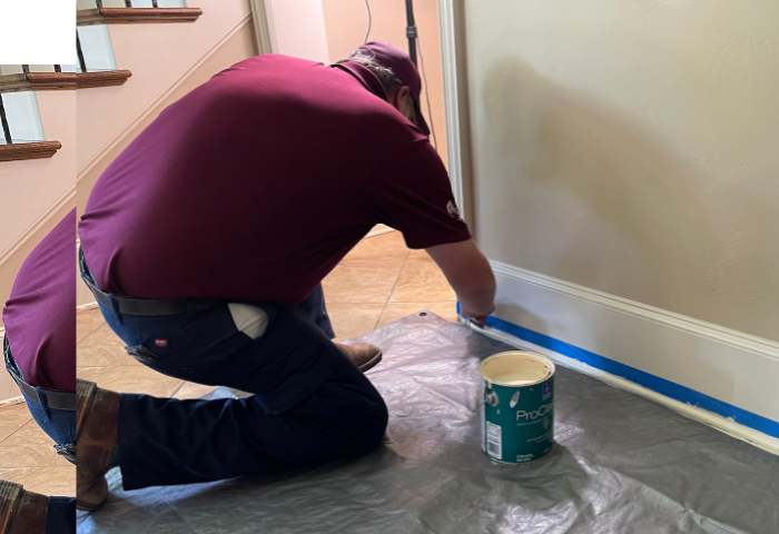 A handyman painting baseboards in a home.