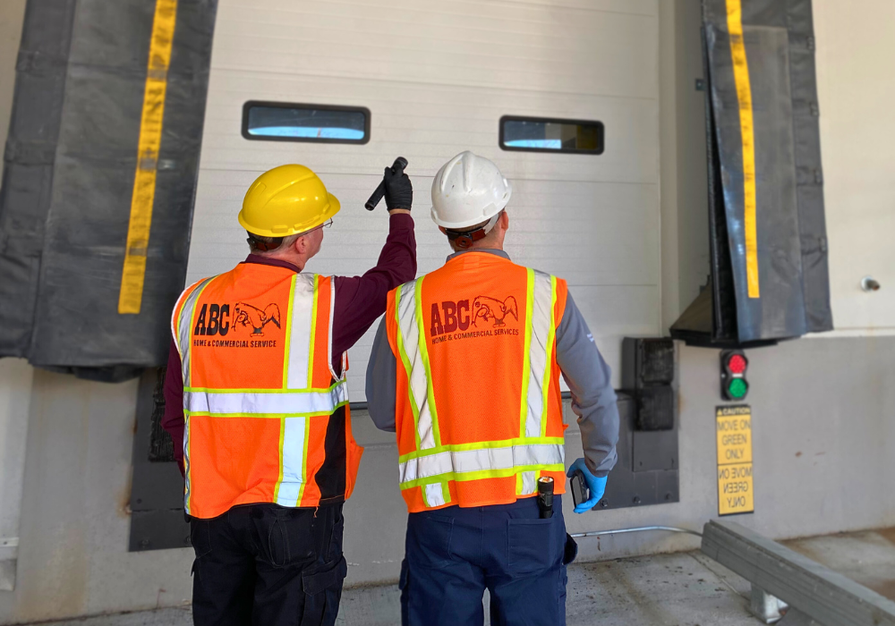 Two ABC commercial specialists inspection a warehouse exterior wearing safety vests.