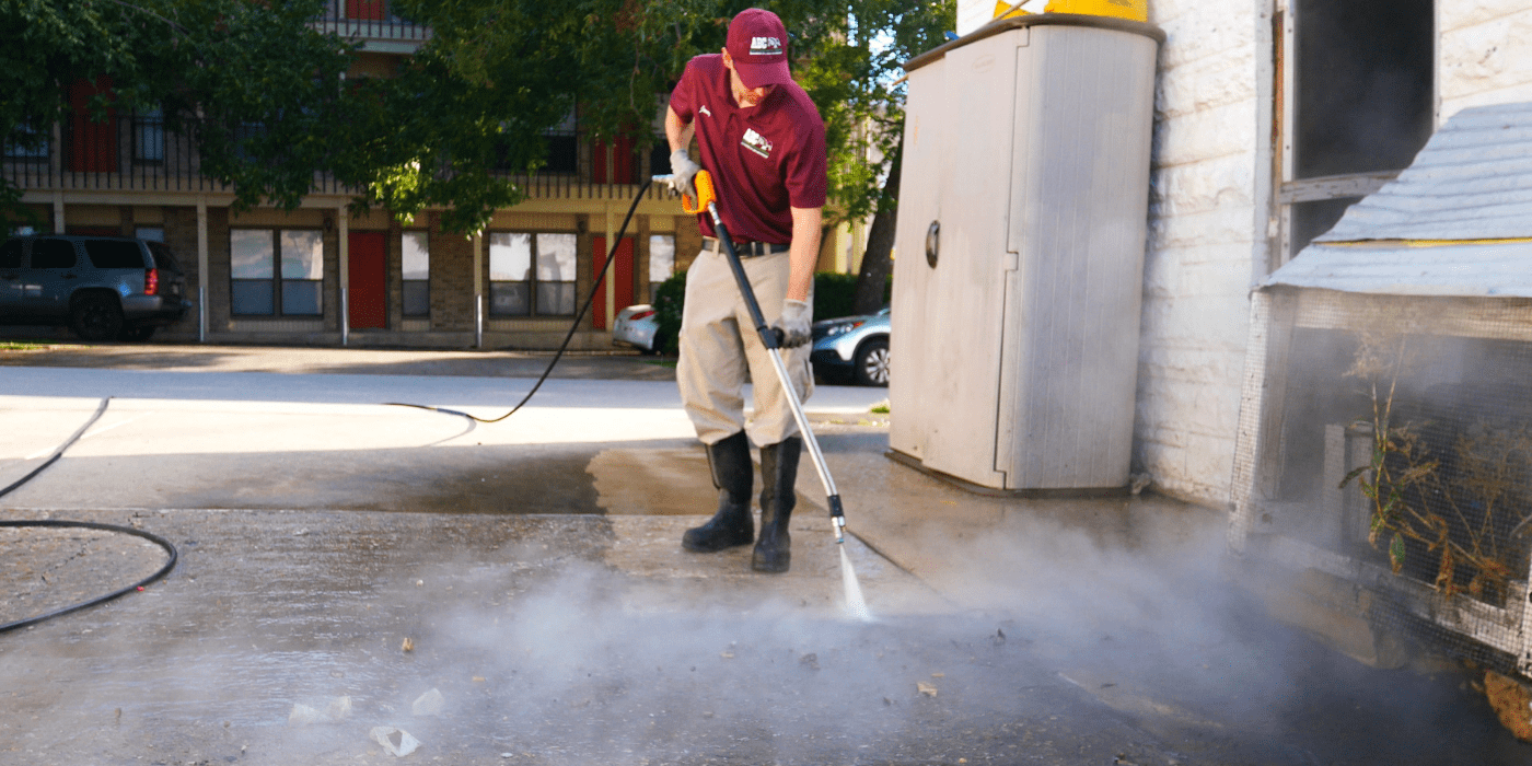 a commercial services specialist power washing a sidewalk outside of a business